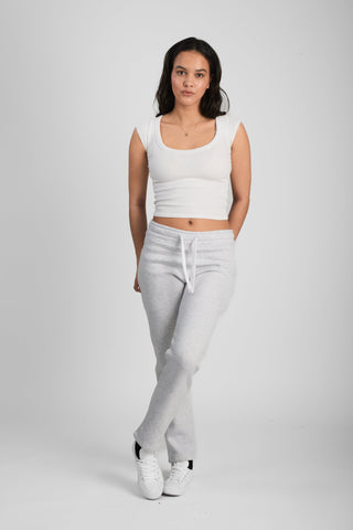Woman wearing a white tank top and light gray pants on a plain background